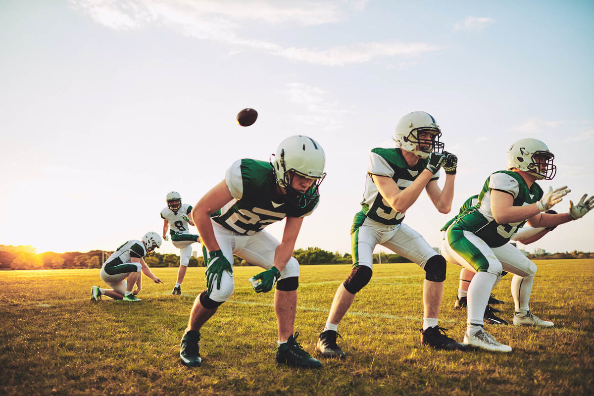 A team of football players at a tryout practicing on the field during sunset