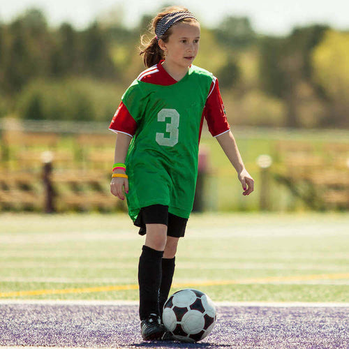 A girl in green and red jersey with number 3 on it, preparing to take her shot with the ball